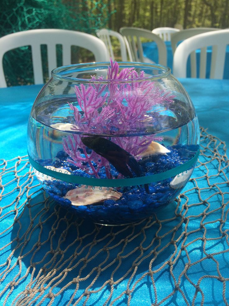 a fish bowl filled with water and corals on top of a blue table cloth