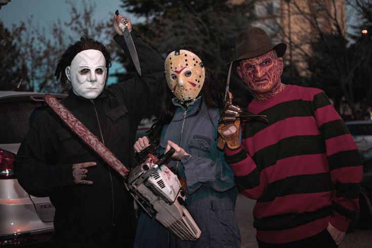 three people dressed up in halloween costumes holding chains and masks on their faces while standing next to a car