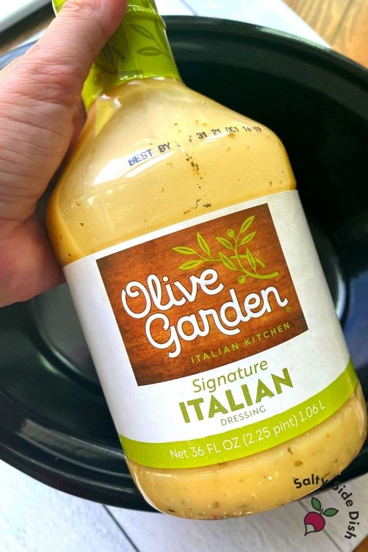 a hand holding a bottle of olive garden sauce