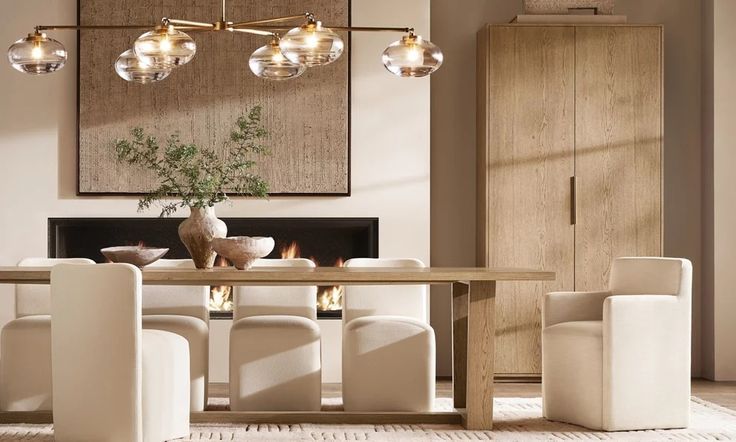 a dining room table with white chairs and lights hanging from it's ceiling over the fire place