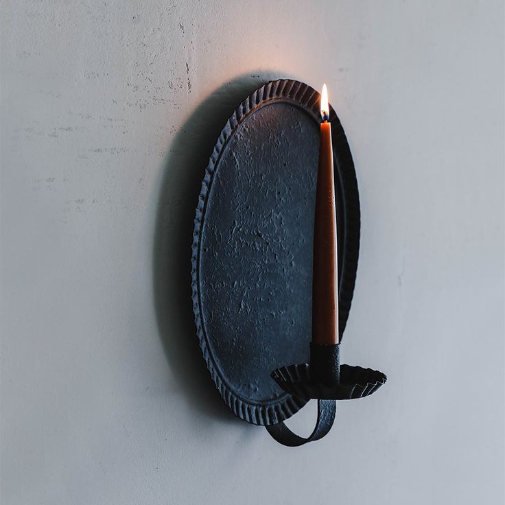 a candle is lit on the wall next to a black plate with a rope around it