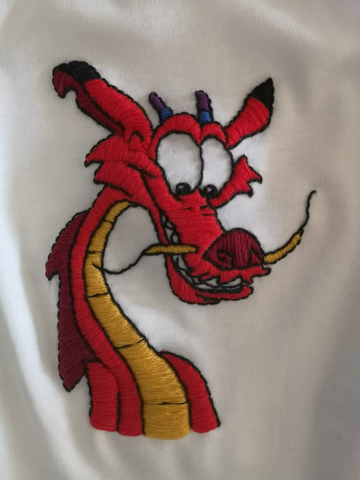 a red dragon embroidered on a white shirt with gold trimmings and a black nose