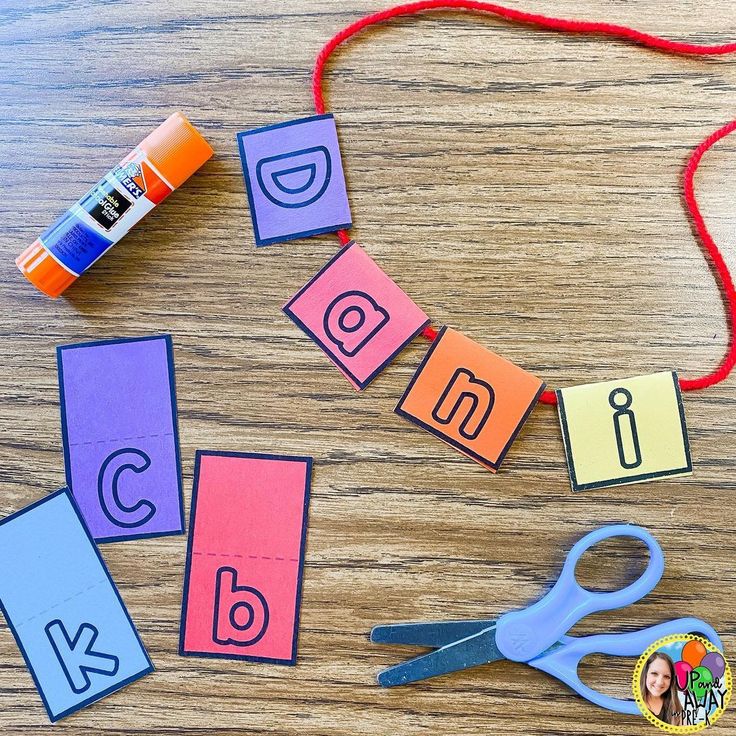 scissors, glue and letters laid out on a wooden table with yarn next to them