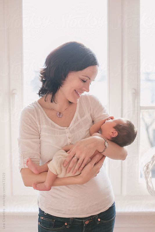 a woman holding a baby in her arms by an open window with sunlight streaming through it