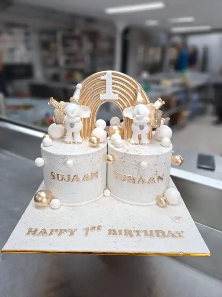 a birthday cake with white frosting and gold decorations on it's sides, sitting in front of a conveyor belt