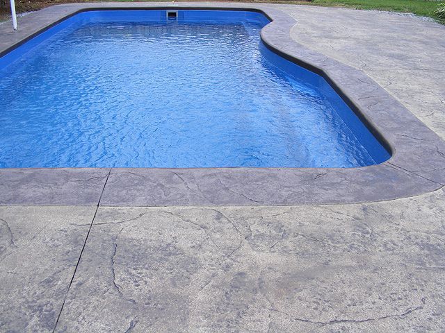 an empty swimming pool in a backyard with concrete pavers and flags on the side