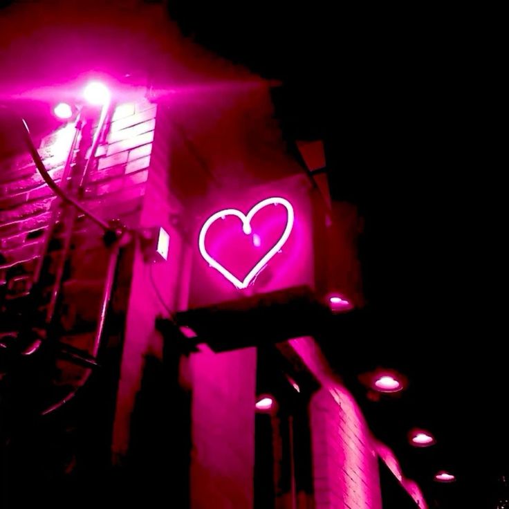 a building with a neon heart on it's side in the dark, lit up at night