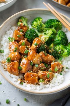 a bowl filled with chicken and broccoli on top of rice next to chopsticks