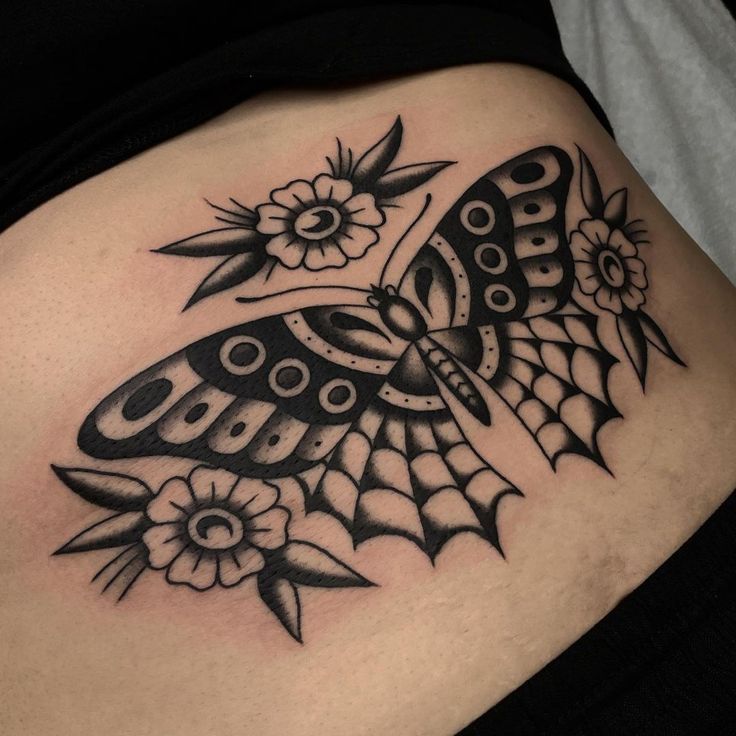 a black and white butterfly tattoo on the side of a woman's stomach with flowers