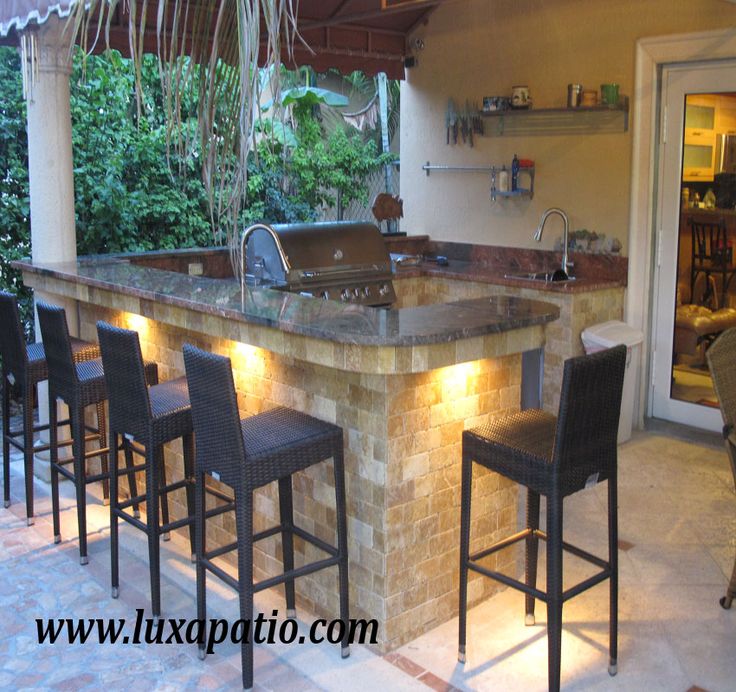 an outdoor bar with stools is lit up by lights and sits on the patio