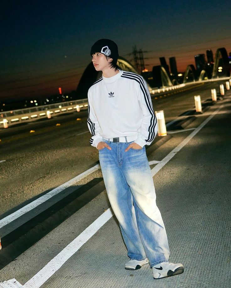 a young man standing in the middle of an empty road at night with his hands on his hips