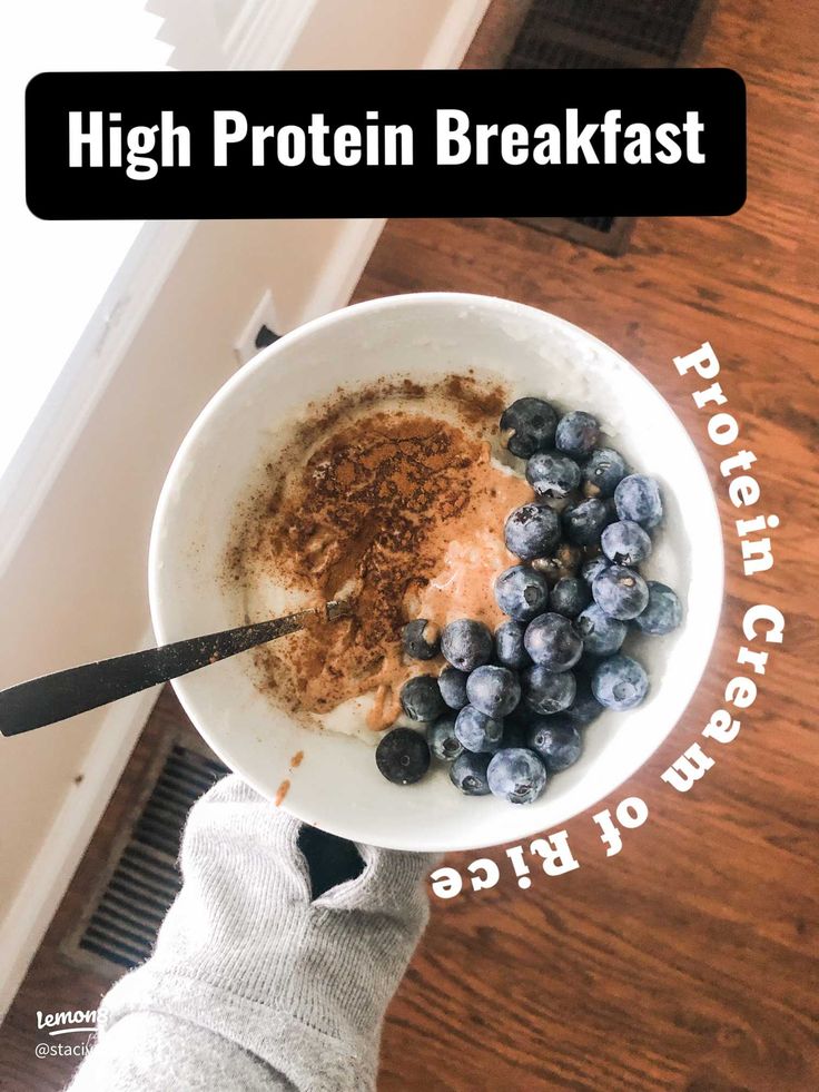 a person holding a bowl of cereal with blueberries and cinnamon in it on top of a wooden table