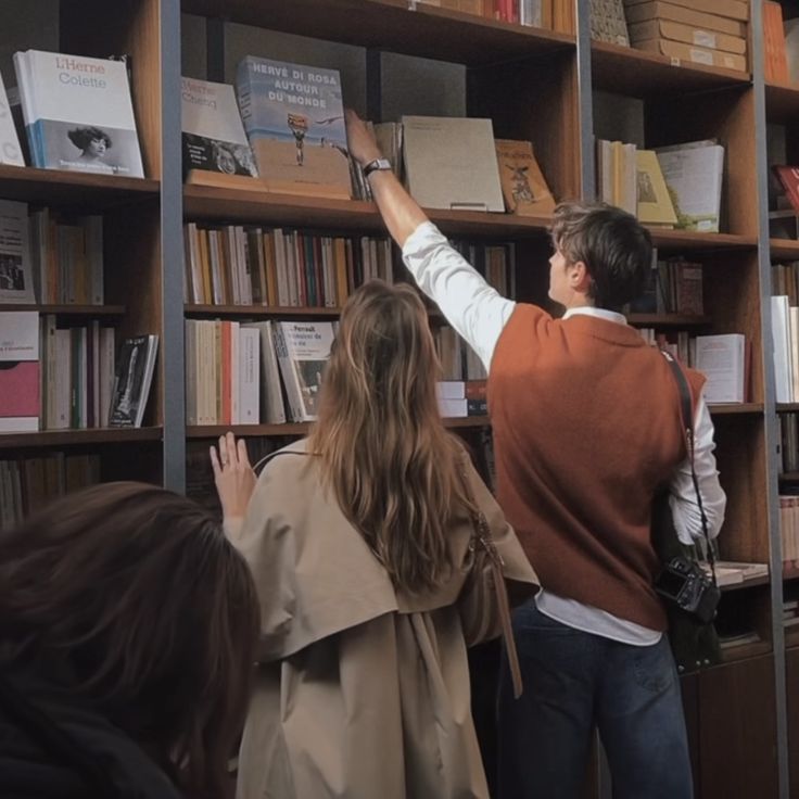 people are looking at books on shelves in a library with one person reaching up for the book