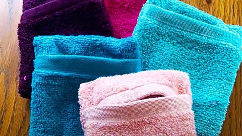 four towels folded on top of each other in different colors and sizes, sitting on a wooden floor