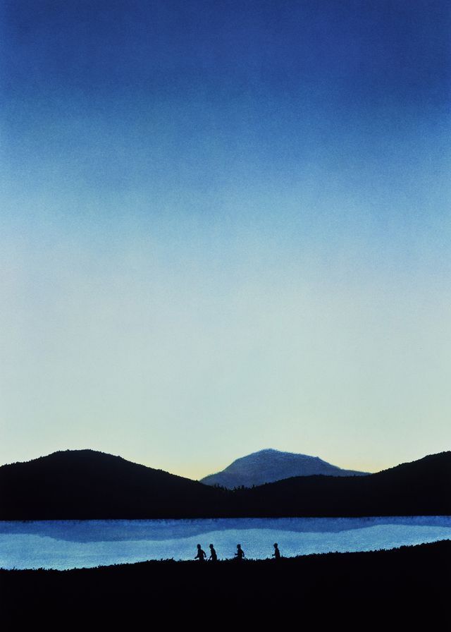 three people are riding their bikes on the shore at dusk with mountains in the background