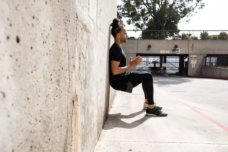 a man sitting on the side of a building next to a cement wall and looking at his cell phone