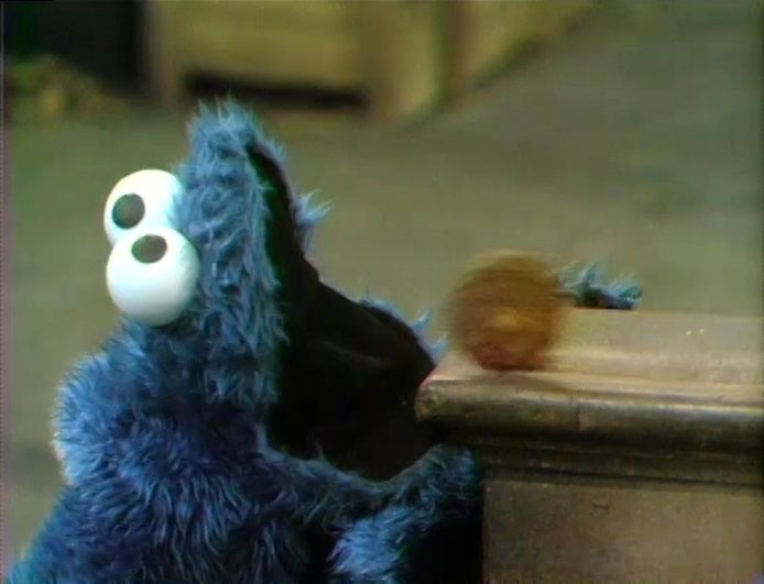 a blue stuffed animal sitting on top of a wooden table next to a wall with eyes