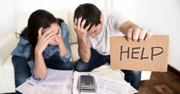 a man and woman sitting on a couch holding up a sign that says help