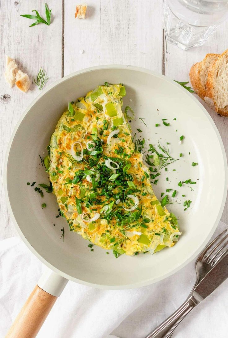 an omelet is served in a white bowl with bread and herbs on the side