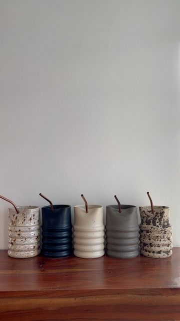 four vases sitting on top of a wooden table next to each other in front of a white wall