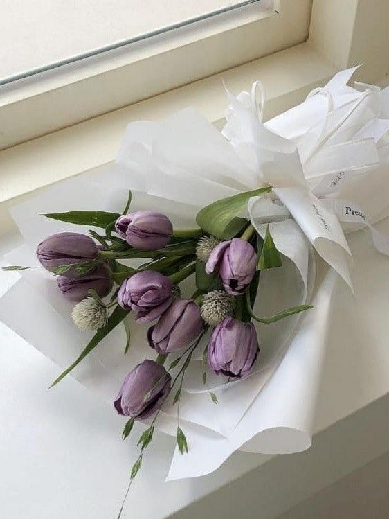 a bouquet of purple tulips wrapped in white paper on a window sill