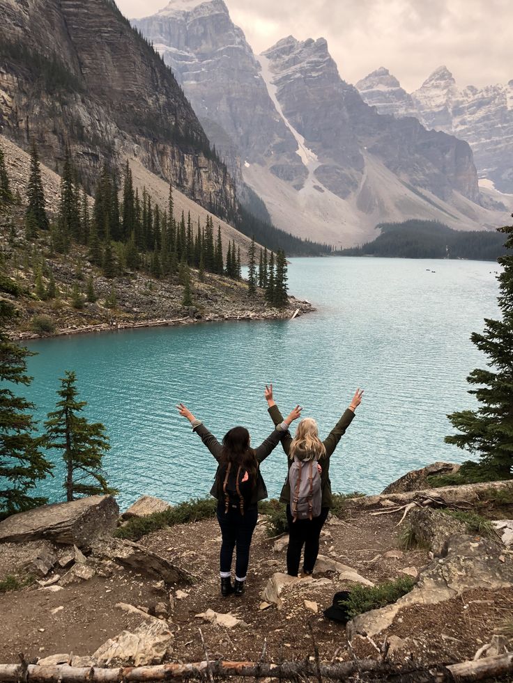 two women standing on the edge of a cliff with their arms in the air