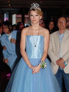 a woman wearing a blue dress and tiara standing in front of other people at an event