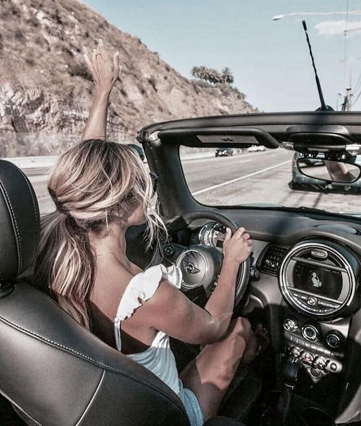 a woman driving a convertible car down a highway