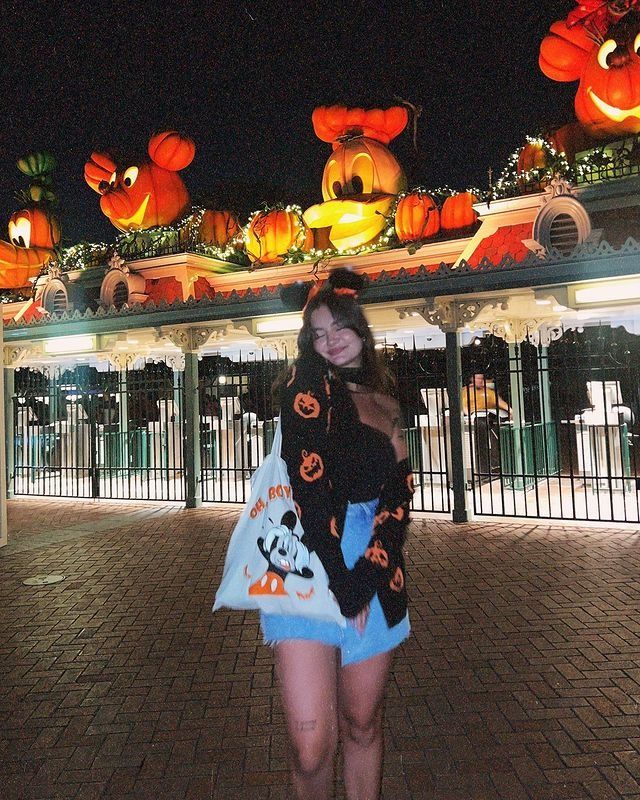 a woman is standing in front of a gate with pumpkins on it at night