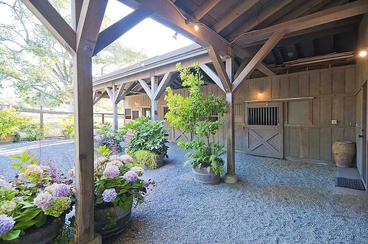 the inside of a barn with lots of plants and flowers in pots on the gravel