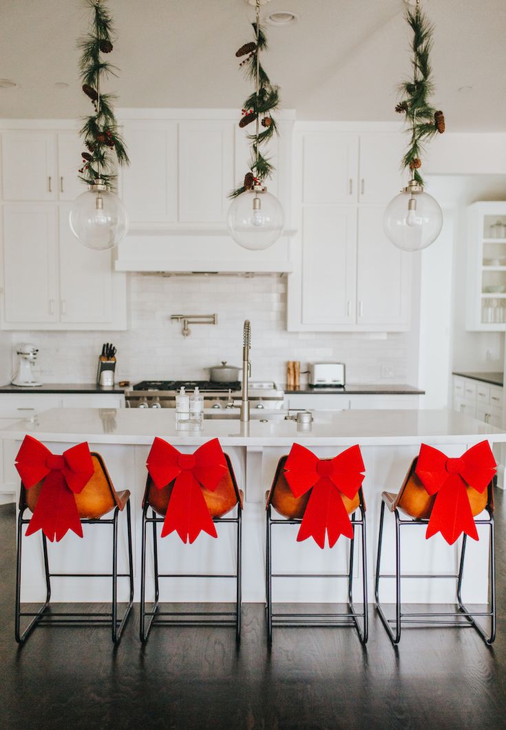 four chairs with bows tied around them in front of a kitchen island and white cabinets