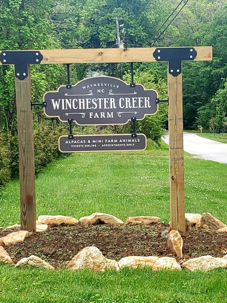 a sign for winchester creek farm in the middle of a grassy area with rocks and trees