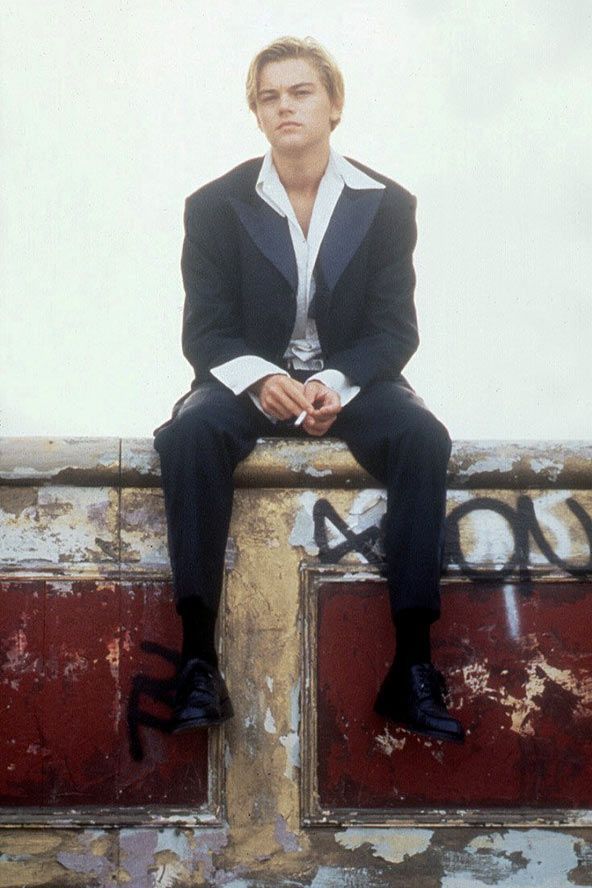 a man in a suit sitting on top of a wooden pole next to graffiti covered wall