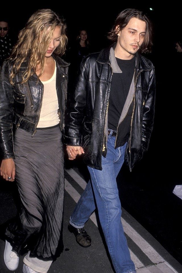 a man and woman walking down the street at night holding hands, both wearing black leather jackets