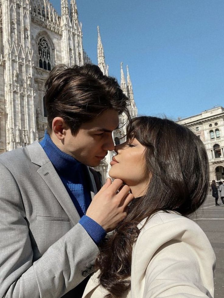 a man and woman standing next to each other in front of a building with tall spires