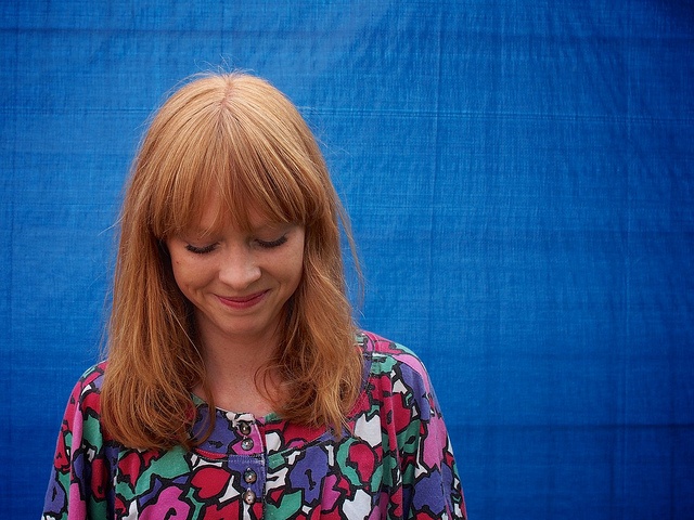 a woman with red hair is looking down at her cell phone while standing in front of a blue backdrop