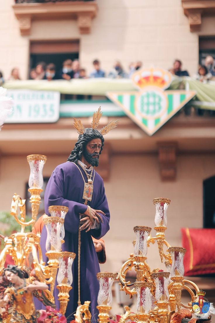 a man dressed in purple is standing next to some gold vases and other items