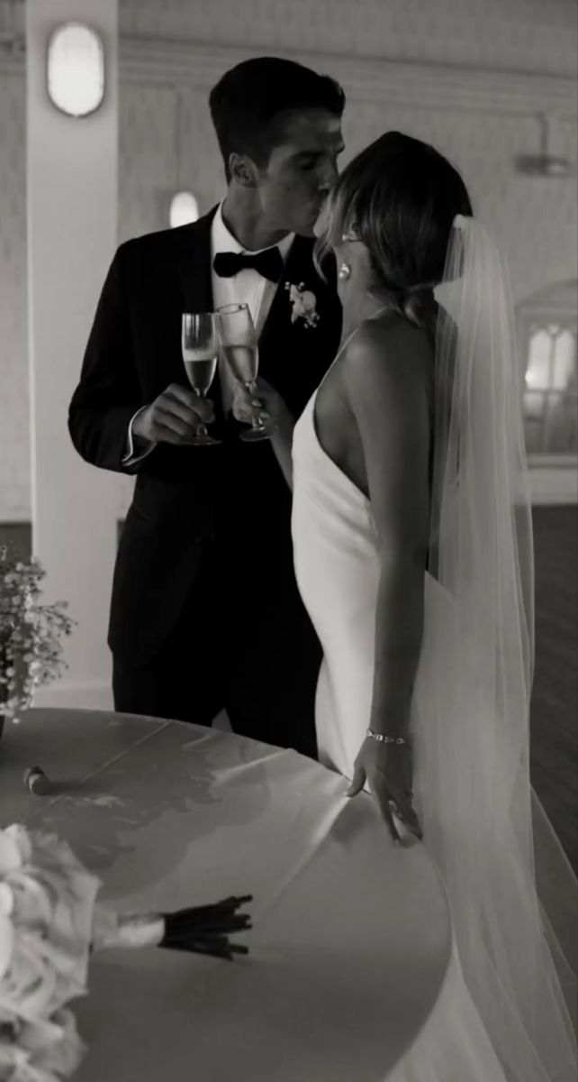 a bride and groom are kissing at their wedding reception in black and white, with the bride holding a glass of champagne