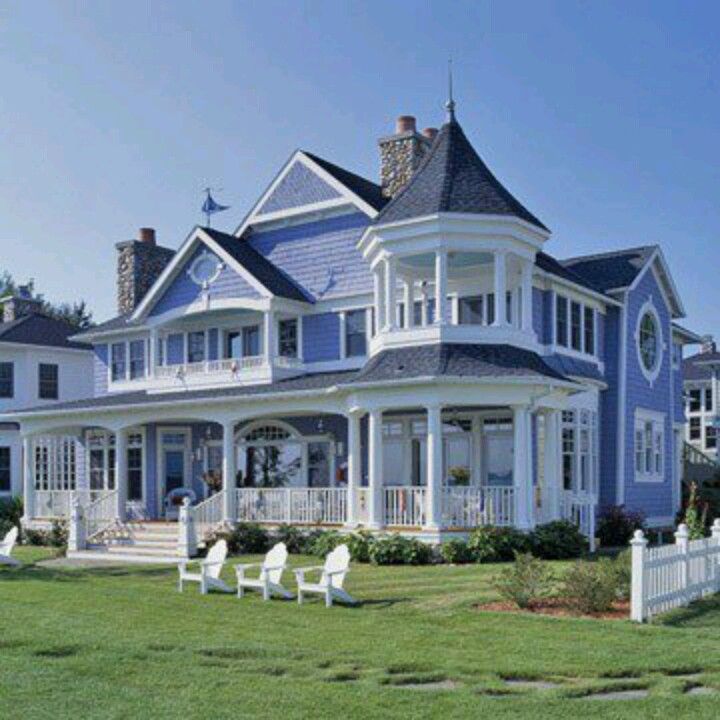 a large blue house with two white chairs in the front yard and an attached porch