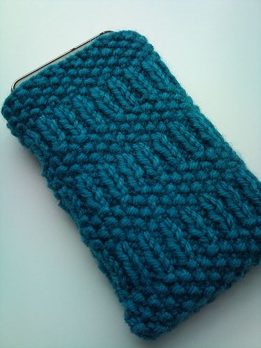 a blue crocheted purse sitting on top of a white table next to a cell phone