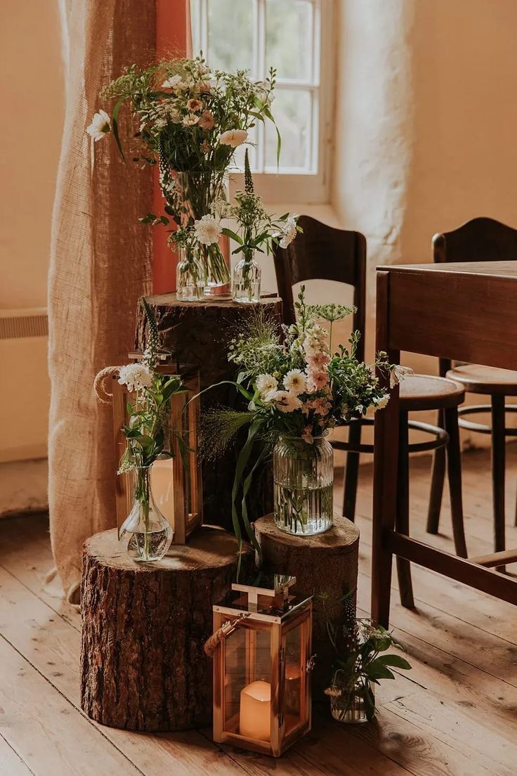 a table topped with vases filled with flowers and greenery next to a window