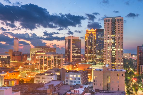 the city skyline is lit up at night with bright lights and clouds in the sky