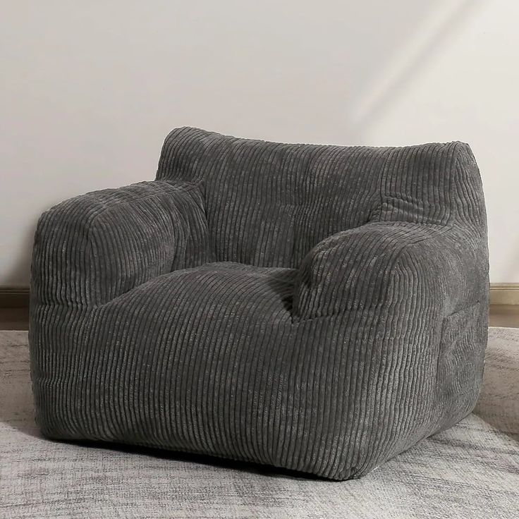 a grey corded chair sitting on top of a rug in front of a white wall