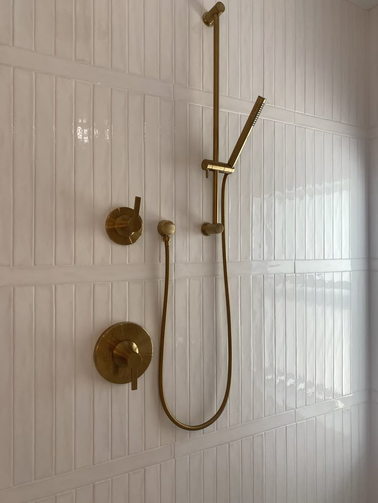 a shower head and hand shower in a white tiled bathroom with gold fixtures on the wall