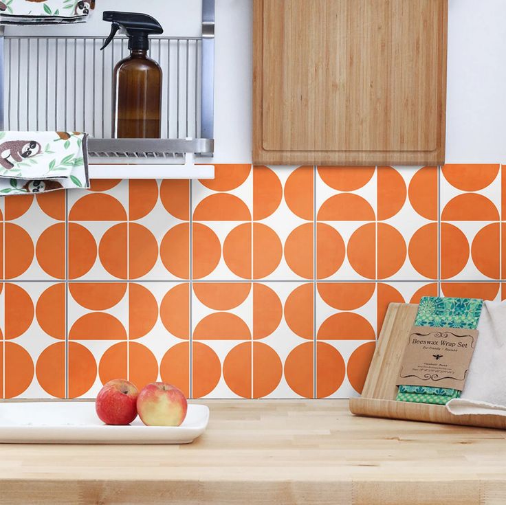 an orange and white tile backsplash in a kitchen with apples on the counter