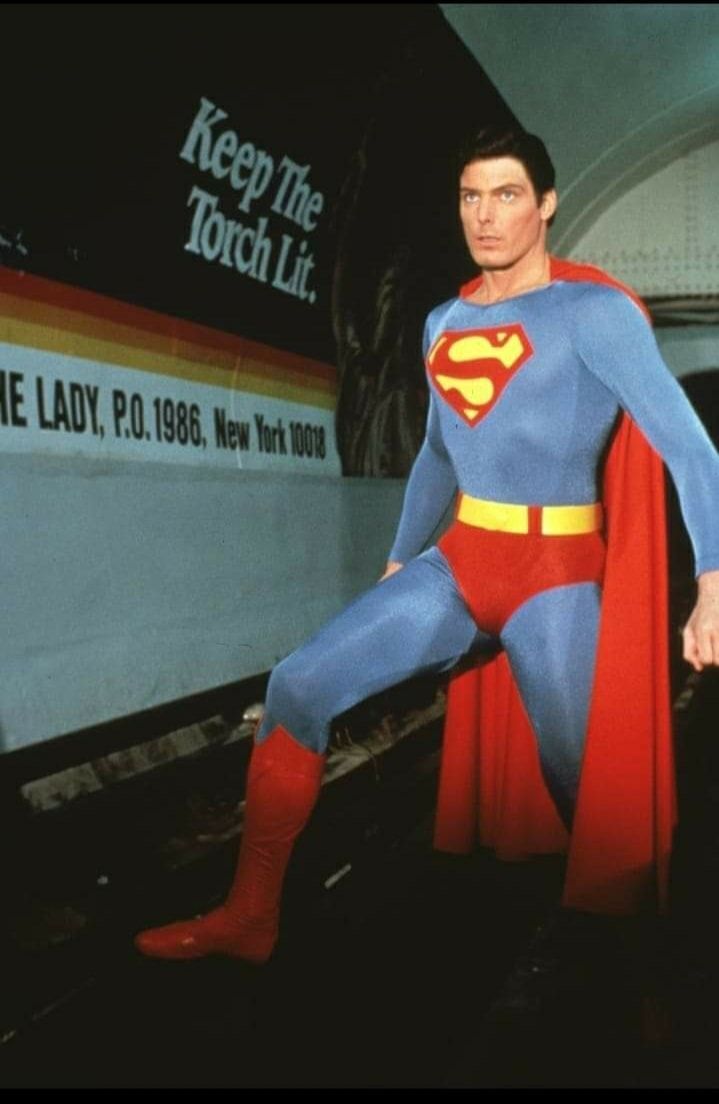 a man dressed as superman poses for a photo in front of a train station sign