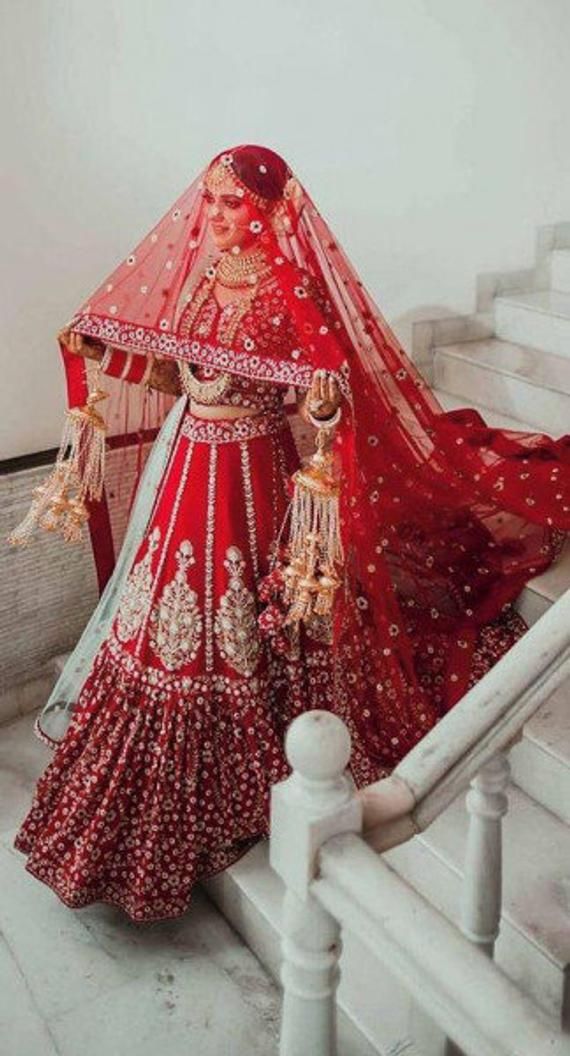 a woman in a red bridal gown and veil walking down stairs with her hands on her hips