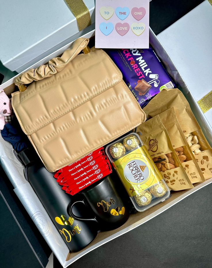 an open box containing coffee, candy and other items on a table next to a laptop