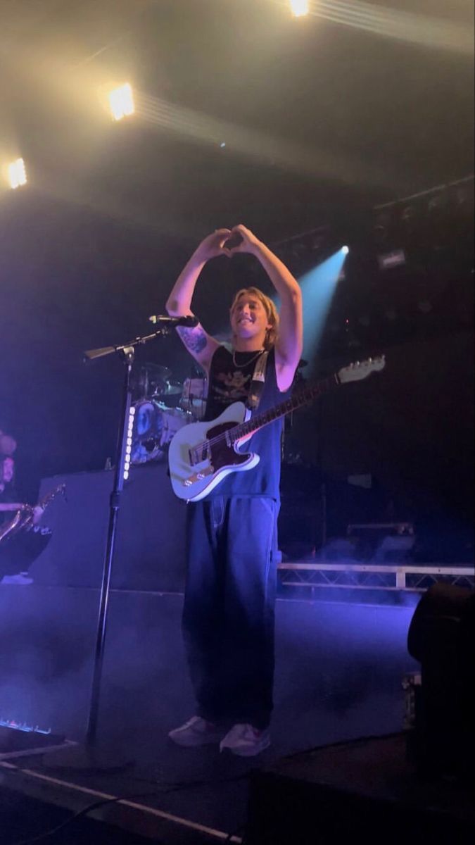 a man standing in front of a microphone on stage with his arms up and holding a guitar