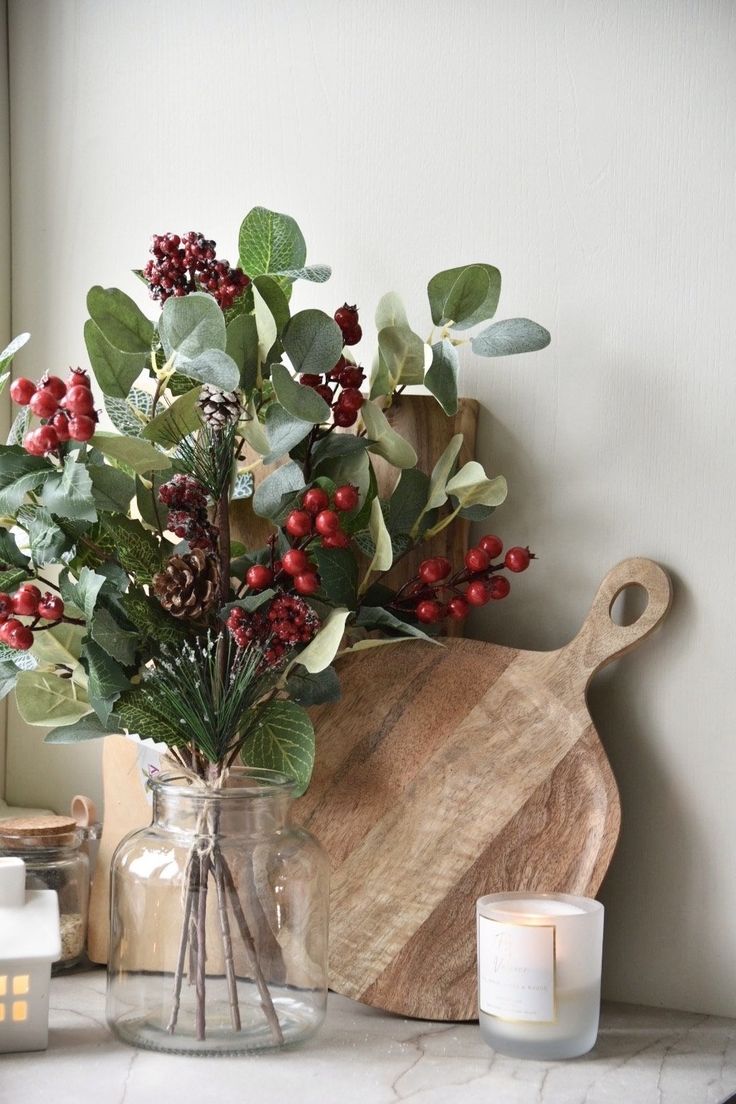 a vase filled with berries and greenery next to a cutting board